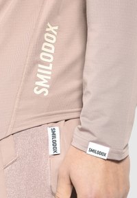 Helles pinkes Sporttop aus strukturiertem Stoff, mit weißem "SMILODOX"-Logo auf der Vorderseite und am Ärmelabschluss.