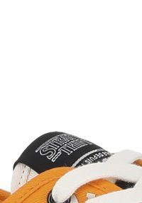 Narančasti teniski s bijelim vezicama, s crnim logotipom na jeziku i teksturiranim platnom, djelomično vidljiv na slici.