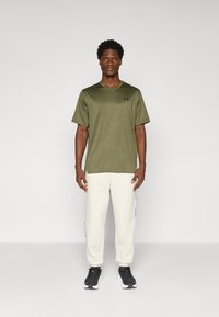 Olivengrønt T-shirt med korte ærmer og rund hals, parret med cremefarvede sweatpants med sorte side-striber og sorte atletiske sko.