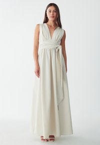 Robe longue couleur crème avec un décolleté en V profond et une ceinture nouée à la taille. Fabriquée en tissu doux, elle possède des panneaux de jupe fluides et longs qui touchent le sol.