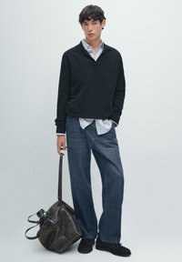 Czarny sweter z pulowerem, jasnoniebieska koszula na guziki, niebieskie dżinsy, czarne buty oraz brązowa skórzana torba z długimi paskami, na neutralnym tle.