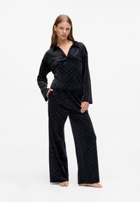 Completo pigiama in velluto nero con una camicia a maniche lunghe con colletto e pantaloni a gamba larga, caratterizzati da una sottile texture a motivo.