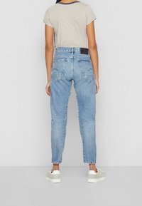 Ljust blå denimjeans med rak passform, fem fickor och subtil blekning. Kombinerat med en randig kortärmad topp och vita sneakers.