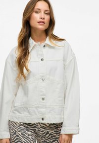 Chaqueta de mezclilla blanca con cuello abotonado, cierre de botones y bolsillos en el pecho. Presenta un corte relajado y una textura suave.