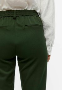 Grønne bukser med elastisk midje og to baklommer, med en glatt tekstur og en taperet bendesign.