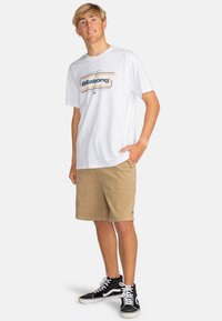 White short-sleeve t-shirt with a printed Billabong logo, paired with beige corduroy shorts and black high-top sneakers.