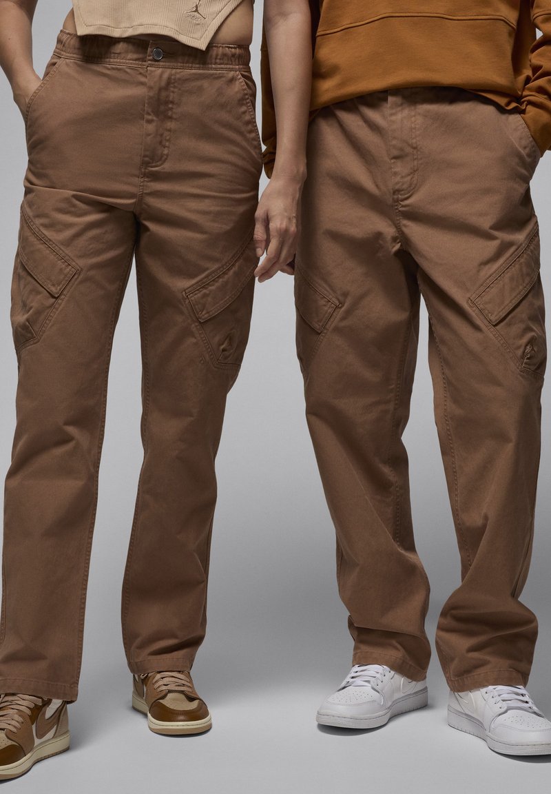 Pantaloni cargo marroni con una vestibilità ampia, dotati di più tasche e una texture del tessuto liscia. Indossati con sneaker in contrasto.
