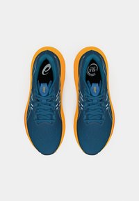 Blauwe sportschoenen met oranje zolen. Kenmerken zijn een gestructureerde bovenkant, witte accentlijnen en ronde veters. Rubberen buitenzool voor grip.