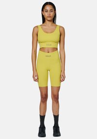 Geel activewear set met een cropped top en high-waisted shorts. Materiaal is glad met HALO branding. Gecombineerd met zwarte sneakers.