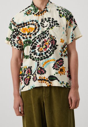 Camicia a maniche corte con bottoni e motivo floreale astratto colorato, indossata con pantaloni di velluto a coste verde oliva.
