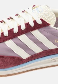 Röda och lavendelfärgade sneakers med paneler i mocka och mesh, klassisk tre-stripdesign, vita snören och en blå mellansula.