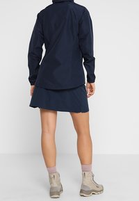 Marinblå vattentät jacka och kjol med en fast struktur. Har långa ärmar, dragkedja fram och kjol som når knäna. Avslutas med khaki vandringskängor.