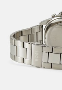 Montre en acier inoxydable argenté avec un bracelet à maillons, dotée d'un fermoir gravé "BOSS". Texture lisse et mate avec des accents polis.