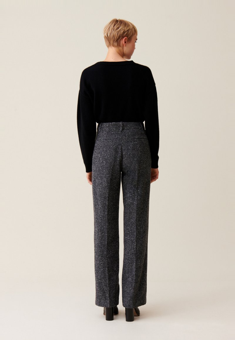 Czarny sweter o luźnym kroju połączony z spodniami o wysokim stanie i szerokich nogawkach, wykonanymi z teksturowanej szarej tkaniny, z delikatnymi plamkami i kieszeniami.