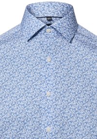 Chemise bleu clair à boutons avec motif paisley, dotée d'un col à pointes et de boutons blancs. Tissu en coton lisse avec une texture subtile.