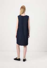 Μπλε ναυτικού, αμάνικο τζιν φόρεμα με ίσια γραμμή, διακριτική ραφή και φερμουάρ στο πίσω μέρος. Τελειώνει στο γόνατο με πλαϊνές σχισμές.