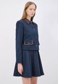 Tmavě modrá pruhovaná sako s hnědým koženým límcem, se zapínáním na knoflíky vpředu a kapsou. V kombinaci s odpovídající rozšířenou sukní.