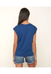 Camiseta azul de manga corta con un corte holgado, escote redondo y puños enrollados, combinada con pantalones cortos de denim claro con bordes deshilachados.