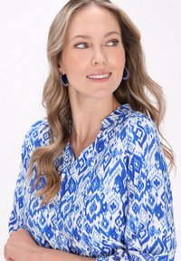 Blusa a maniche lunghe blu e bianca con scollo a V, realizzata in un tessuto morbido e decorata con un motivo di forme geometriche.