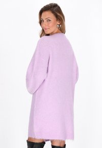 Vaalean liila neuletta oversized -kardigania, jossa on pehmeä rakenne, pitkät hihat ja sivuhalkiot. Koristeelliset yksityiskohdat hihoissa.