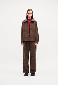 Brown corduroy jacket with large front pockets, button closure, and a shirt collar, paired with matching brown wide-leg pants and black shoes.