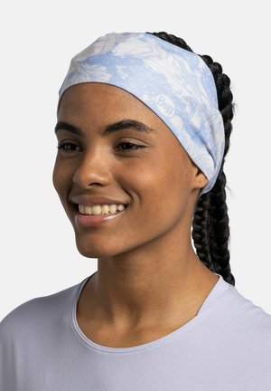 Smiling woman with braided hair wearing a light blue floral headband and lavender athletic shirt against white background.
