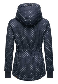 Veste marine à pois blancs, taille cintrée et capuche. Comprend des poignets élastiques et un branding discret sur le bord inférieur. Matériau imperméable.