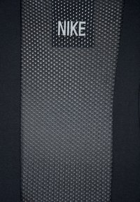 Svart atletisk tyg har ett strukturerat nätmönster med små diamantskulpturer; en Nike-tag är synlig i mitten högst upp.