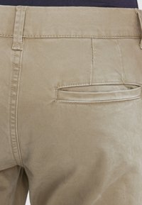 Beżowe bawełniane spodnie o gładkiej fakturze, z tylną kieszenią przeszytą nicią w tym samym kolorze i prostym paskiem w pasie.