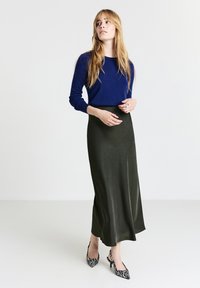 Pull marin à manches longues associé à une longue jupe maxi en soie vert foncé avec une texture élaborée et des escarpins zèbre noir et blanc.
