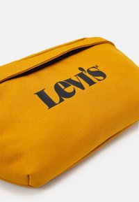 Sacchetto di stoffa giallo texturizzato con logo nero Levi's e chiusura con cerniera su uno sfondo bianco.