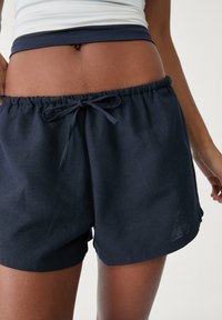 Námořnické modré šortky na šňůrku vyrobené z lehkého materiálu s elastickým pasem a jemnou texturou, s klasickým střihem a neformálním stylem.