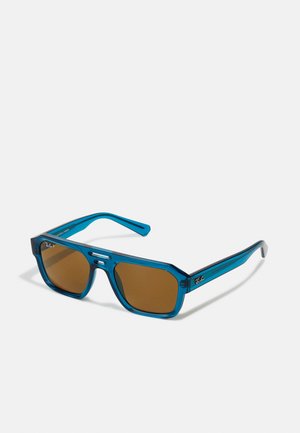 Occhiali da sole blu trasparenti con lenti marroni, forma ottagonale e design elegante. Presentano dettagli argentati e il logo Ray-Ban sul lato.