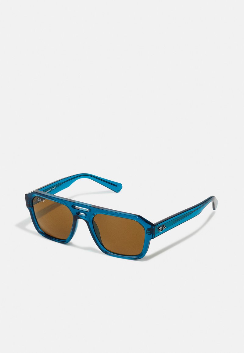 Ochelari de soare transparenți blue cu lentile maro, formă octagonală și design elegant. Prezintă accente argintii și logo-ul Ray-Ban pe lateral.