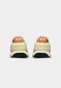 Beige semskinn og mesh sneakers med oransje detaljer, med polstret krage, logo på hælen og en teksturert svart gummisåle.