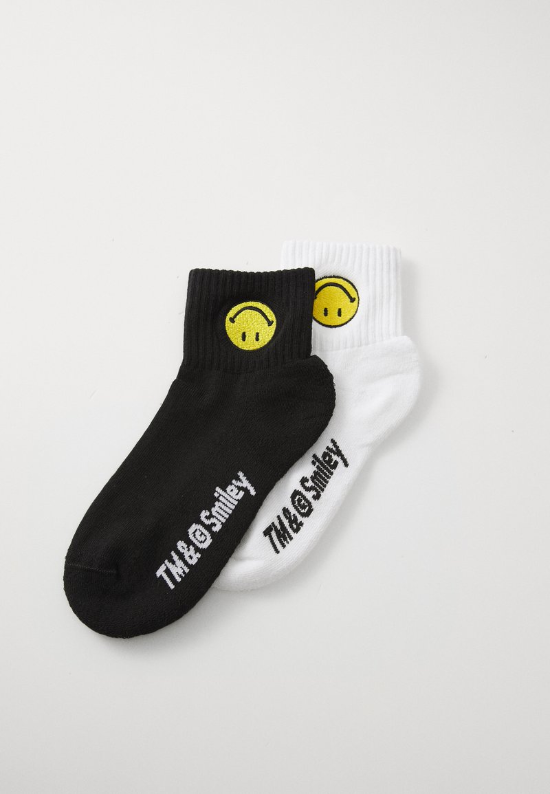 Black and white crew socks featuring a yellow smiley face logo. Ribbed texture, with "TM & Smiley" printed on the black sock.