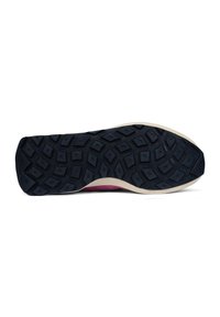 Sole of a shoe with a textured black rubber surface featuring multi-directional grooves, bordered by a cream-colored edge.