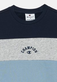 Camiseta de manga corta Champion en azul marino, gris claro y azul. Presenta un cuello redondo y un logotipo bordado en el pecho. Material de algodón suave.