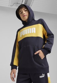 Mėlynos ir geltonos spalvos gobtuvas su dideliu baltu "PUMA" logo. Yra priekinė kišenė, rankogaliai ir minkšta medžiagos tekstūra.