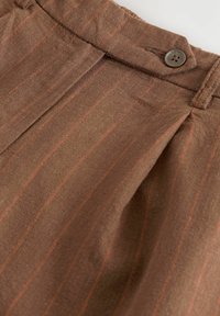 Pantaloni in lino marrone con righe arancioni verticali, dotati di pieghe e di un solo bottone marrone. Texture liscia e design della vita su misura.