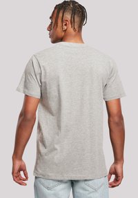 Grå bomull t-skjorte med korte ermer, rund hals, og en jevn tekstur, sett fra bak. Brukt med lyseblå jeans.