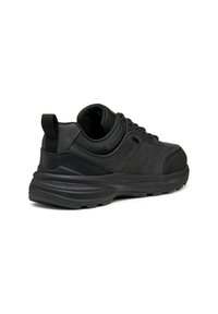 Scarpa sportiva nera che mostra una combinazione di materiali lisci e testurizzati, punta arrotondata, suola rialzata e un linguetta sul retro per facilitare l'indosso.