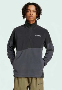 Μαύρο και γκρι φλις πόλο με ψηλό γιακά, μπροστινό φερμουάρ και λογότυπο TERREX στο στήθος; διαθέτει μαλακή υφή και αθλητική εφαρμογή.