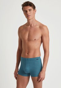 Herenboxershorts in een tealblauw patroon met geometrische designs. Het materiaal is soepel met een fitted vorm en een elastische tailleband.