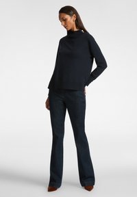 Marinblå pulloversweater med mock neck och sidoknappar, kombinerad med mörk tvättade utsvängda jeans. Slät textur och avslappnad passform.