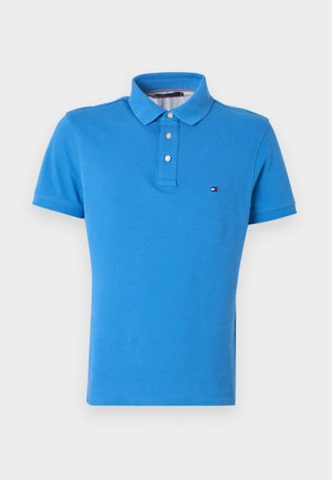 Sinine puuvillane polotees klassikalise kraega, kolme nupu ja väikese rinnale tikitud logoga. Lühikesed varrukad, sile pind.