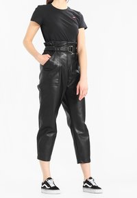 Černé tričko s malým červeným logem, černé kalhoty z umělé kůže s vysokým pasem a pásem, a černobílé tenisky.