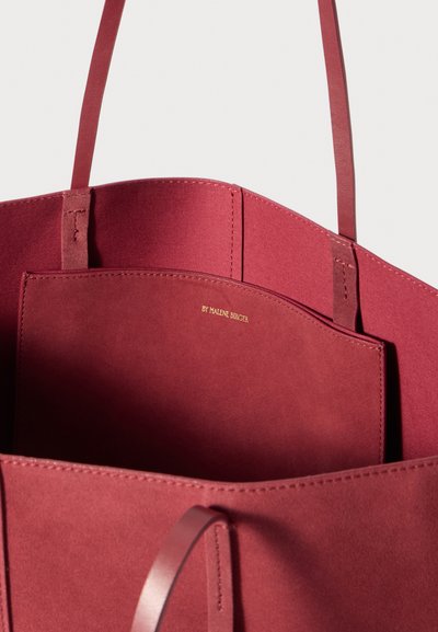 Burgundy tote bag with smooth suede-like texture, featuring a flat interior pocket and detailed stitching. Handle straps are sleek and minimalist.