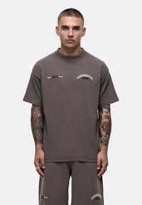 T-shirt grigia oversize, collo a giro, maniche corte, con testo bianco stampato sul petto. Materiale in cotone morbido. Abbinata a pantaloni corti coordinati.