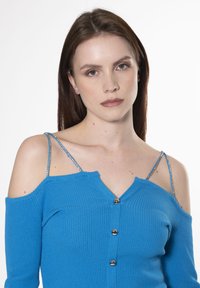 Top azzurro brillante a coste con spalle scoperte, chiusura con bottoni e dettagli lucidi sulle spalline. Presenta un scollo a V e una texture morbida.